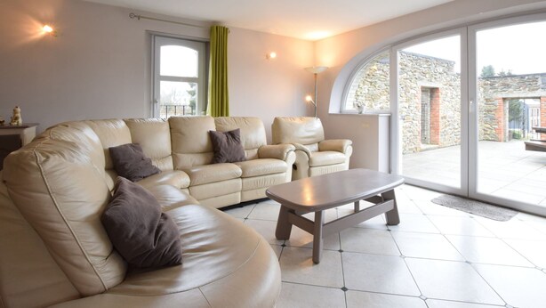 A modern living room with a beige leather sofa, a wooden coffee table, and a large sliding glass door leading to an outdoor area.