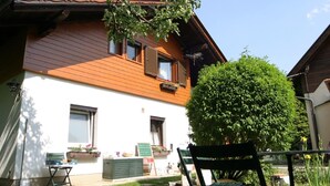 A two-story house with a wooden exterior and white walls. There is a green lawn in front, a bench, and a small table with a basket. - Lovely Holiday Home near Wernberg (Wernberg)