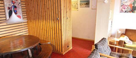 A room with a wooden slatted partition, a round dining table with benches, and a sofa with patterned cushions.