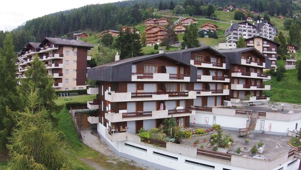 A multi-story hotel with balconies, a parking area, and a view of surrounding buildings and hills. - Apartment Near the Ski Lifts (Riddes)