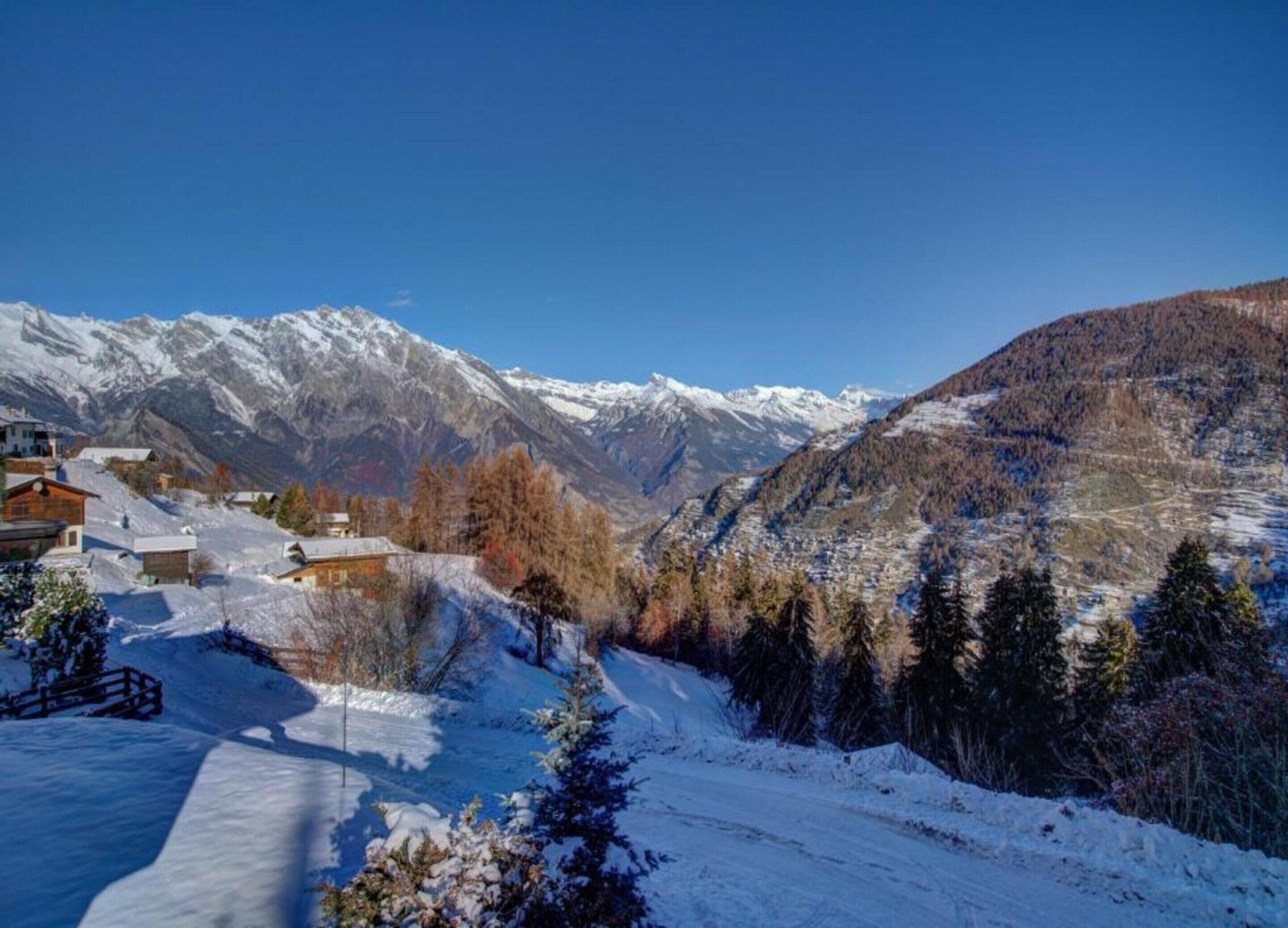 A mountainous landscape with snow-covered peaks and a valley with buildings.