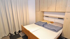 A small, compact room with a bed, a wooden wardrobe, and a checkered floor. - Apartment Near the Ski Lifts (Riddes)