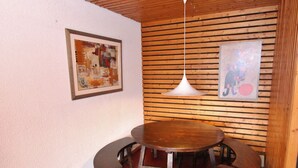 A dining area with a round wooden table and four chairs, a hanging pendant light, and two framed artworks on the walls. - Apartment Near the Ski Lifts (Riddes)