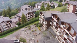 A multi-story hotel with balconies, a parking area, and a view of surrounding hills. - Apartment Near the Ski Lifts (Riddes)