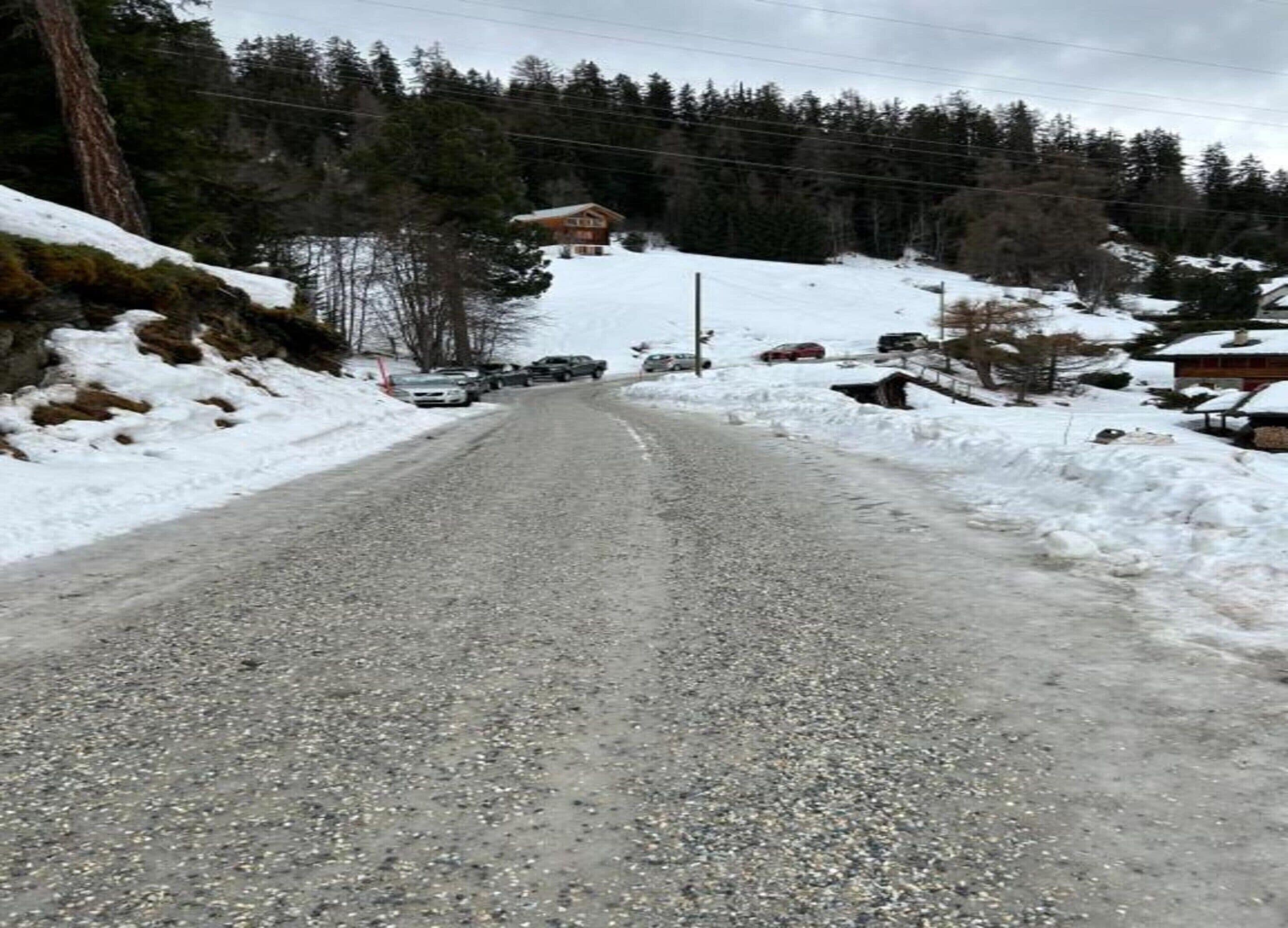Uma estrada de cascalho ladeada por encostas cobertas de neve e vegetação rala.
