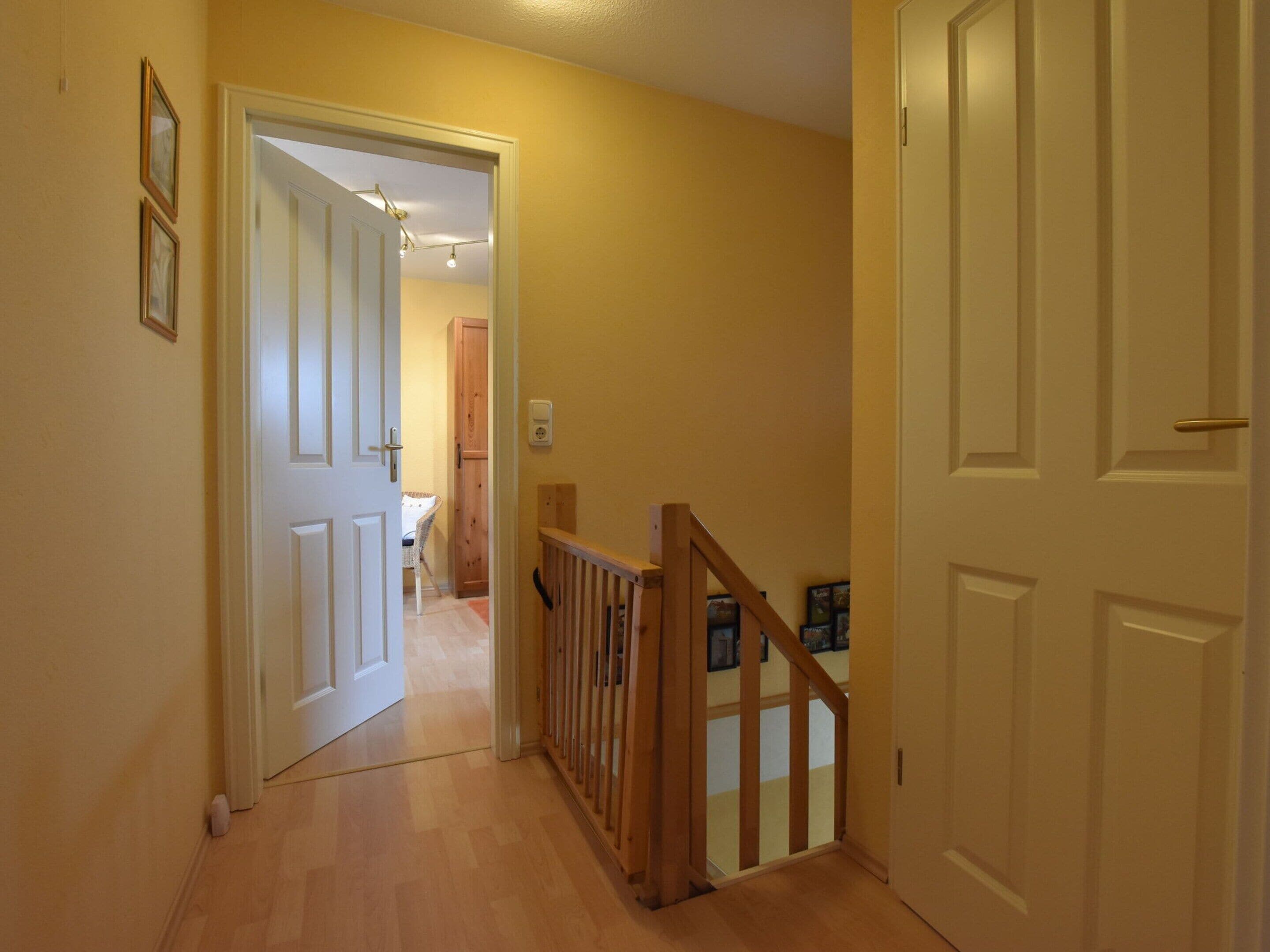 A hallway with wooden flooring, white doors, and a wooden railing.
