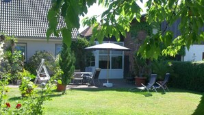 Un jardin avec une terrasse, une pelouse et une maison dont le toit est recouvert de tuiles.