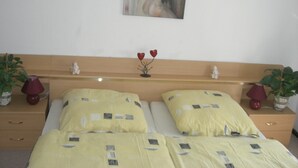 Une chambre avec une tête de lit en bois, deux lits avec une literie jaune, un petit vase avec des fleurs rouges et deux plantes en pot, une de chaque côté du lit.