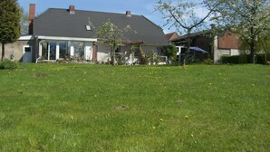 Une maison avec un toit en pente, un porche à l’avant et une pelouse parsemée de fleurs jaunes.