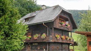 Um edifício de madeira rústico com varanda decorada com flores, um banco de madeira e uma placa com o texto "Haus Blocher".