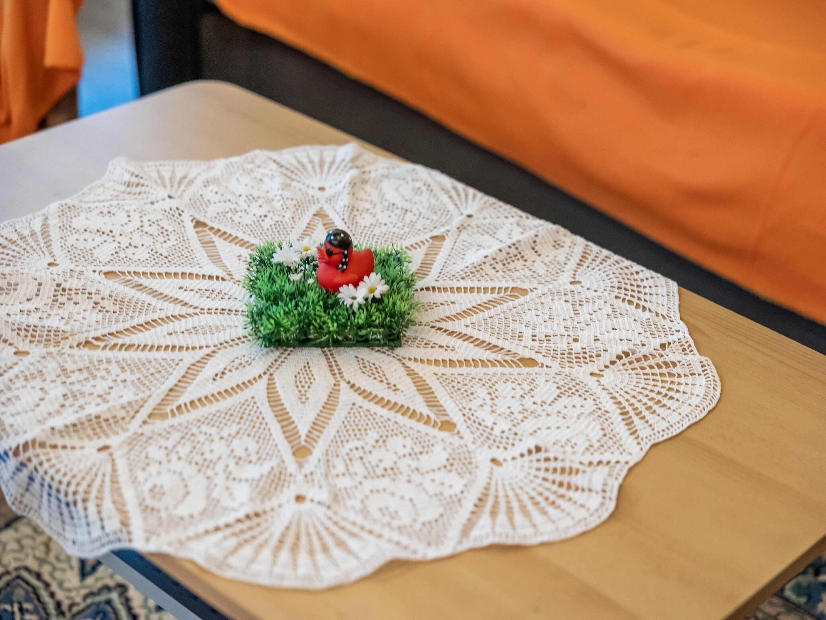 Un encaje blanco de crochet con una pequeña figurita sobre una mesa de madera.