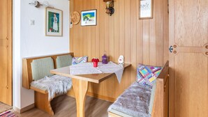 Una habitación acogedora con paneles de madera, un banco de madera con un plaid de piel, una mesa con mantel blanco y una pequeña alfombra en el suelo.