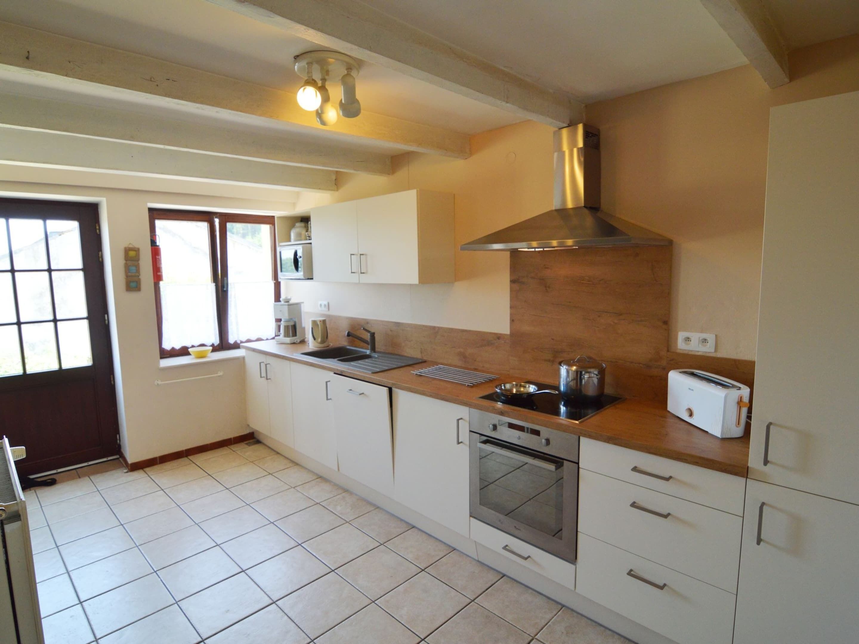 A kitchen with white cabinets, a stainless steel range hood, a built-in oven, a toaster, and a window with a view.