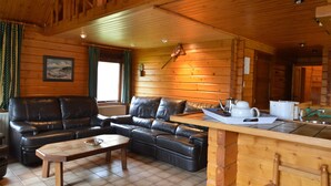 A cozy cabin interior with a leather sofa, wooden dining table, and a kitchen area with a sink and countertop. - Scenic Chalet in Ovifat (Waimes)