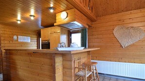 A wooden cabin interior with a kitchen area, a heart-shaped wall decoration, and a wooden bar stool. - Scenic Chalet in Ovifat (Waimes)