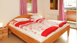 Une chambre avec un lit en bois, des rideaux roses, une fenêtre donnant sur un beau paysage et un radiateur.