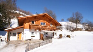 Un chalet en bois doté d’un balcon, d’une entrée couverte et surplombant un paysage enneigé.