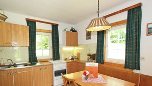 A kitchen with wooden cabinets, a stove, a sink, and a dining table with chairs. - Historic Holiday Home in Gmünd near Cross Country Skiiing (Gmuend in Kaernten)
