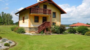 A two-story house with a balcony, a stone foundation, and a well-maintained lawn. - Country House in Czech Forest With Pool (Horní Kozolupy)