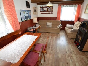 Un salon chaleureux avec un plancher en bois, deux canapés, une table avec des chaises, une cheminée et un téléviseur.