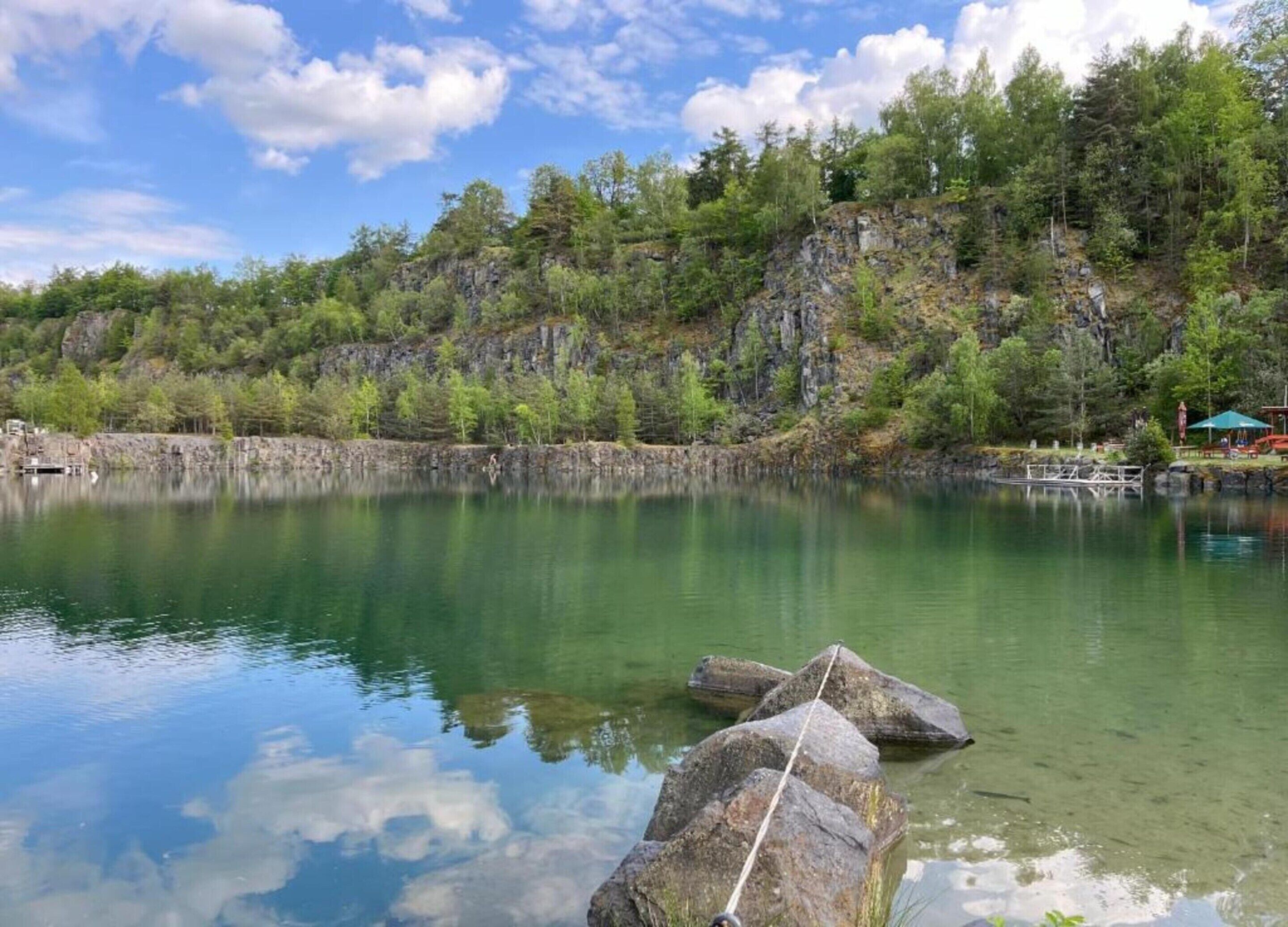A calm lake with clear water, surrounded by rocky cliffs and dense trees.