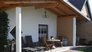 Une terrasse couverte avec une table et des chaises, un luminaire suspendu et un mur en briques.