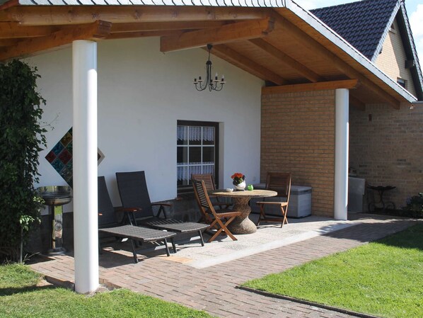 A covered patio with a table and chairs, a hanging light fixture, and a brick wall. - Ferienwohnung, Ostseebad Rerik (Rerik)