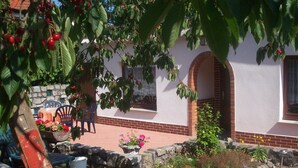 A house with a stone wall, a brick foundation, and a garden with flowers and a tree with red fruits. - Bungalow in Alt Bukow Near the Beach (Alt Bukow)