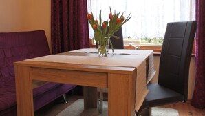 A room with a wooden table, a purple sofa, a black chair, and a window with curtains. - Bungalow in Alt Bukow Near the Beach (Alt Bukow)