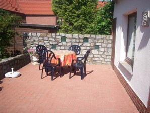 An outdoor patio with a stone wall, a table with chairs, and a small white object on the ground. - Bungalow in Alt Bukow Near the Beach (Alt Bukow)