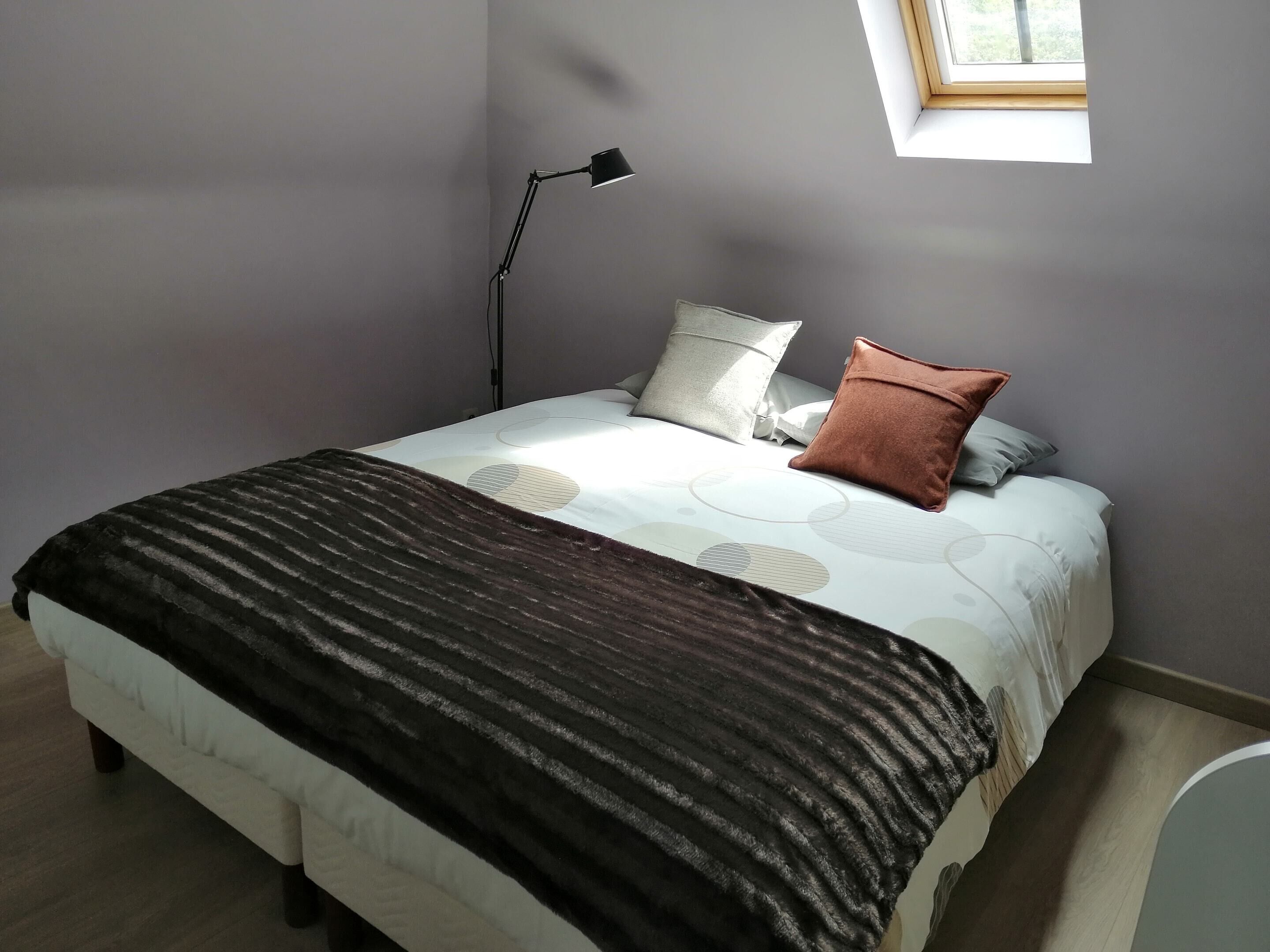 A bedroom with a bed, pillows, a bedside lamp, and a window.
