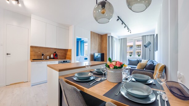 A modern kitchen with white cabinets, a wooden countertop, and a dining area with a wooden table set for four. - Apartamenty Sun & Snow Zielone Tarasy (Kolobrzeg)