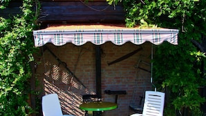 A patio area with two white plastic chairs and a small round table, covered by a plaid awning. - Modern Apartment With Garden, Terrace, Barbecue and Heating (Wendorf)