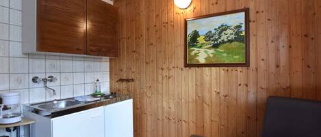 A compact kitchen with wooden cabinets, a sink, and a painting of a landscape.