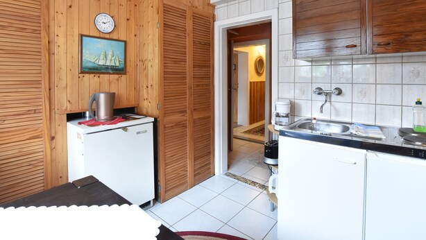 A compact kitchen with wooden paneling, a small refrigerator, a coffee maker, and a sink. - Ferienwohnung im Ostseebad Kuhlungsborn (Kuehlungsborn)