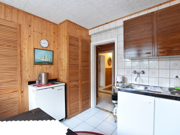 Ett kompakt kök med träpanel, ett litet kylskåp, en kaffebryggare och ett handfat.