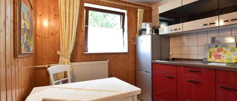 A wooden-paneled room with a dining table and chairs, a refrigerator, and a kitchen with red cabinets.