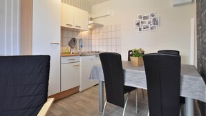A modern kitchen with white cabinets, a tiled backsplash, and a dining area with a table and chairs. - Peaceful Bungalow in Diedrichshagen near Baltic Sea (Kroepelin)