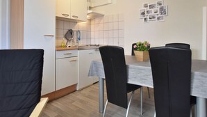 A compact kitchen with white cabinets, a sink, and a dining area with a table and chairs. - Peaceful Bungalow in Diedrichshagen near Baltic Sea (Kroepelin)