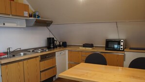 A compact kitchen with wooden cabinets, a dishwasher, a microwave, and a small dining area with two chairs. - Wohnung an der Ostseekuste (Wendorf)