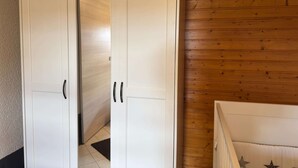 A room with a white wardrobe, wooden flooring, and a white bed with star patterns.