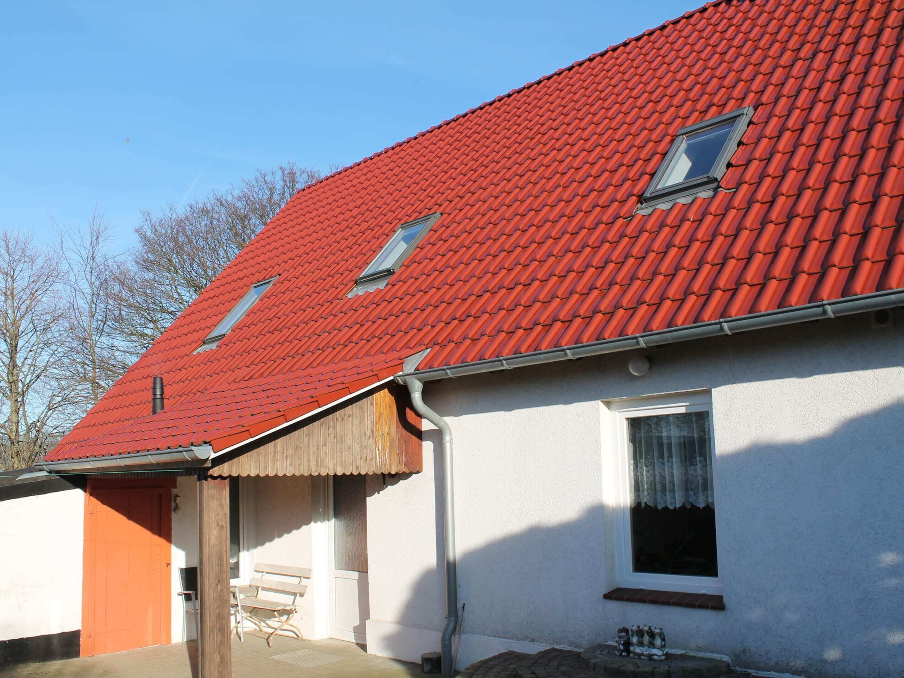 A house with a red-tiled roof, a wooden door, and a small porch with a bench.