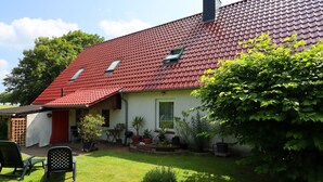 A house with a red tiled roof, a small porch, and a garden with potted plants and a lawn chair. - Ferienwohnung in Brusow an der Ostseekueste (Kroepelin)