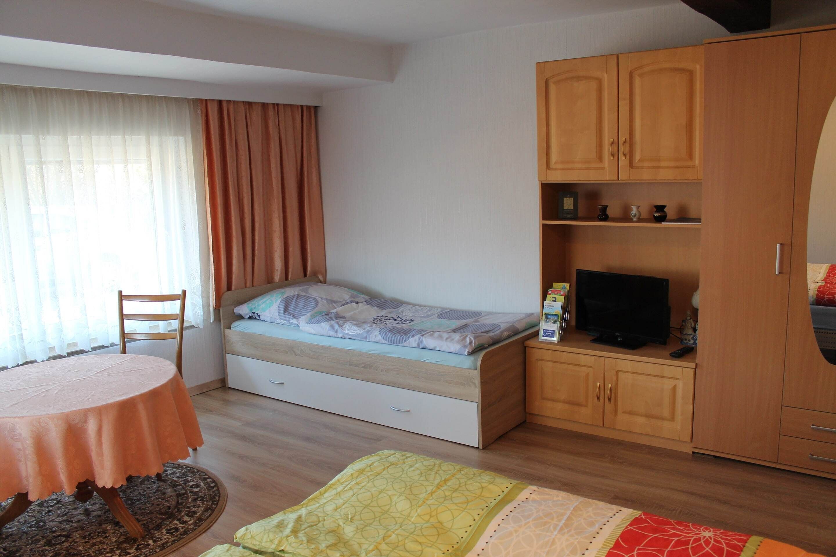 Un dormitorio pequeño con una cama individual, una mesita, un televisor y un armario.