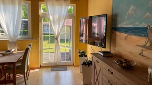 Ein Zimmer mit einem Holzesstisch, Stühlen, einem an der Wand befestigten Fernseher und einem Bild mit einer Strandansicht.