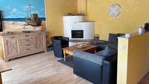 Ein gemütliches Wohnzimmer mit Holzbalkendecke, einem Bild mit Strandmotiv, einem Kamin, einer Couch und einem Couchtisch.