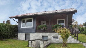 Uma casa de dois andares com fachada de pedra, varanda de madeira com corrimão e um pequeno jardim.