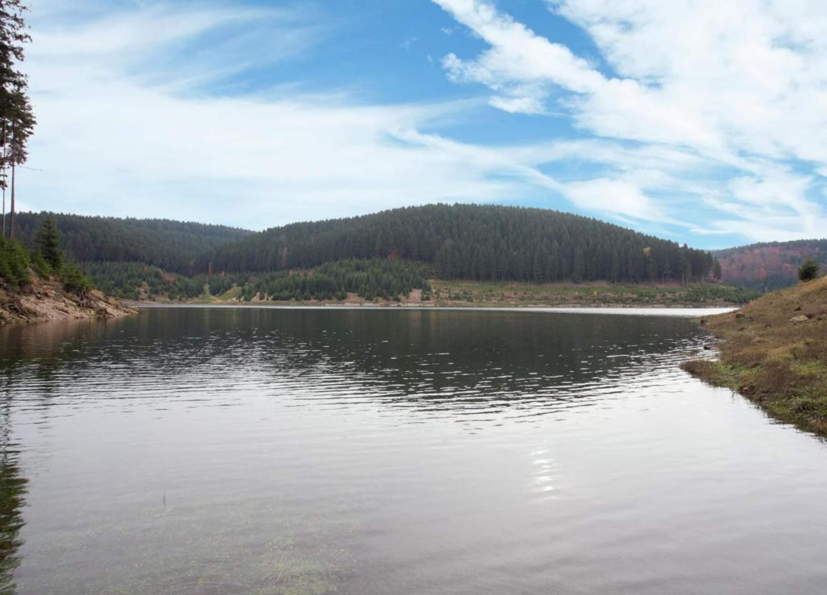 A calm lake surrounded by forested hills under a partly cloudy sky.