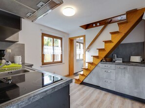 A modern kitchen with a built-in stove, a wooden staircase, and a window with a view of the outside. - Ferienhaus im Thuringer Wald (Wutha-Farnroda)