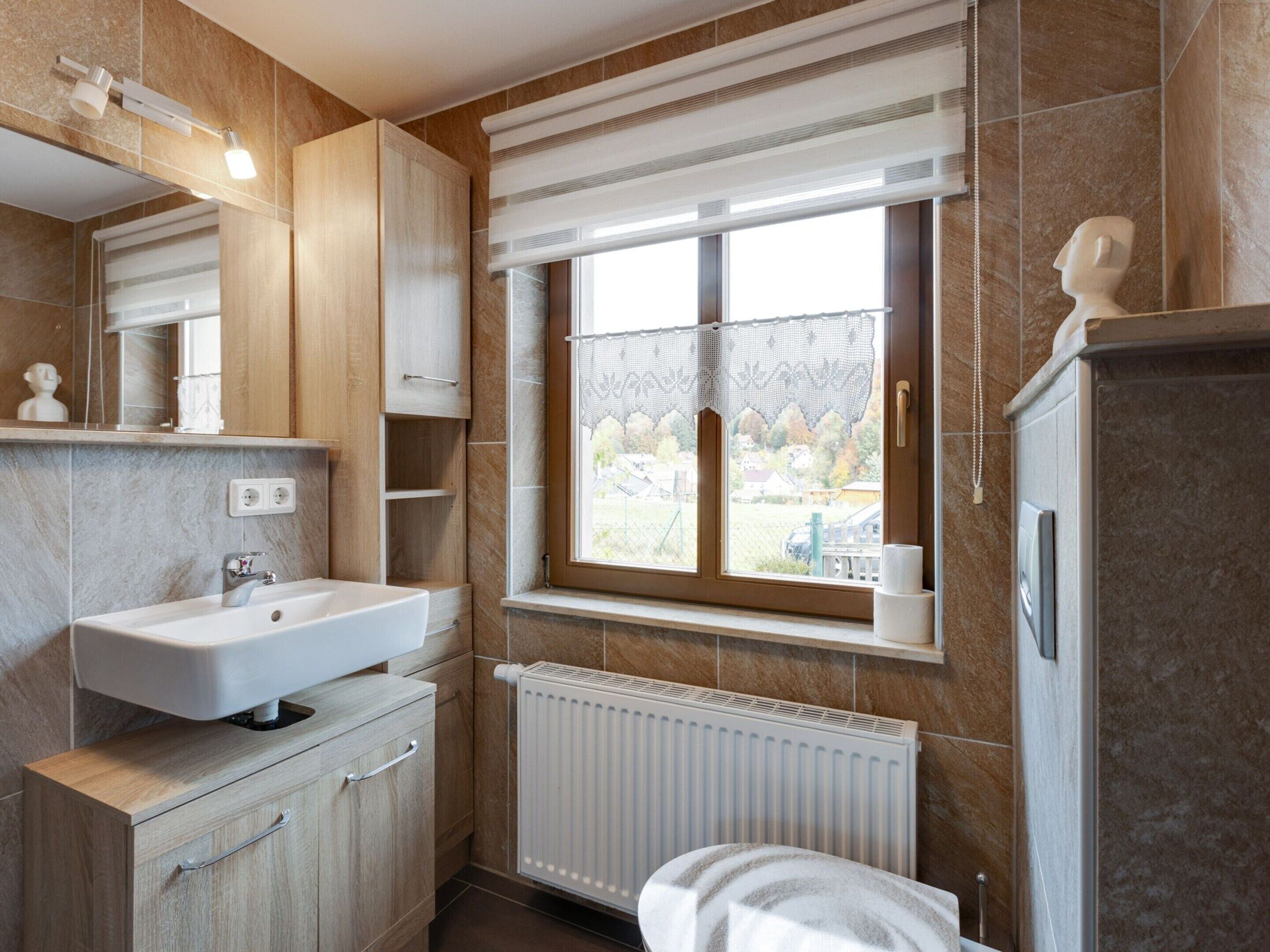 A modern bathroom with a built-in sink, wooden cabinets, a window with a view, and a radiator.